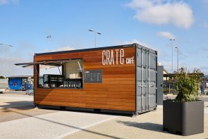 a shipping container cafe wrapped in wooden cladding with an open serving window