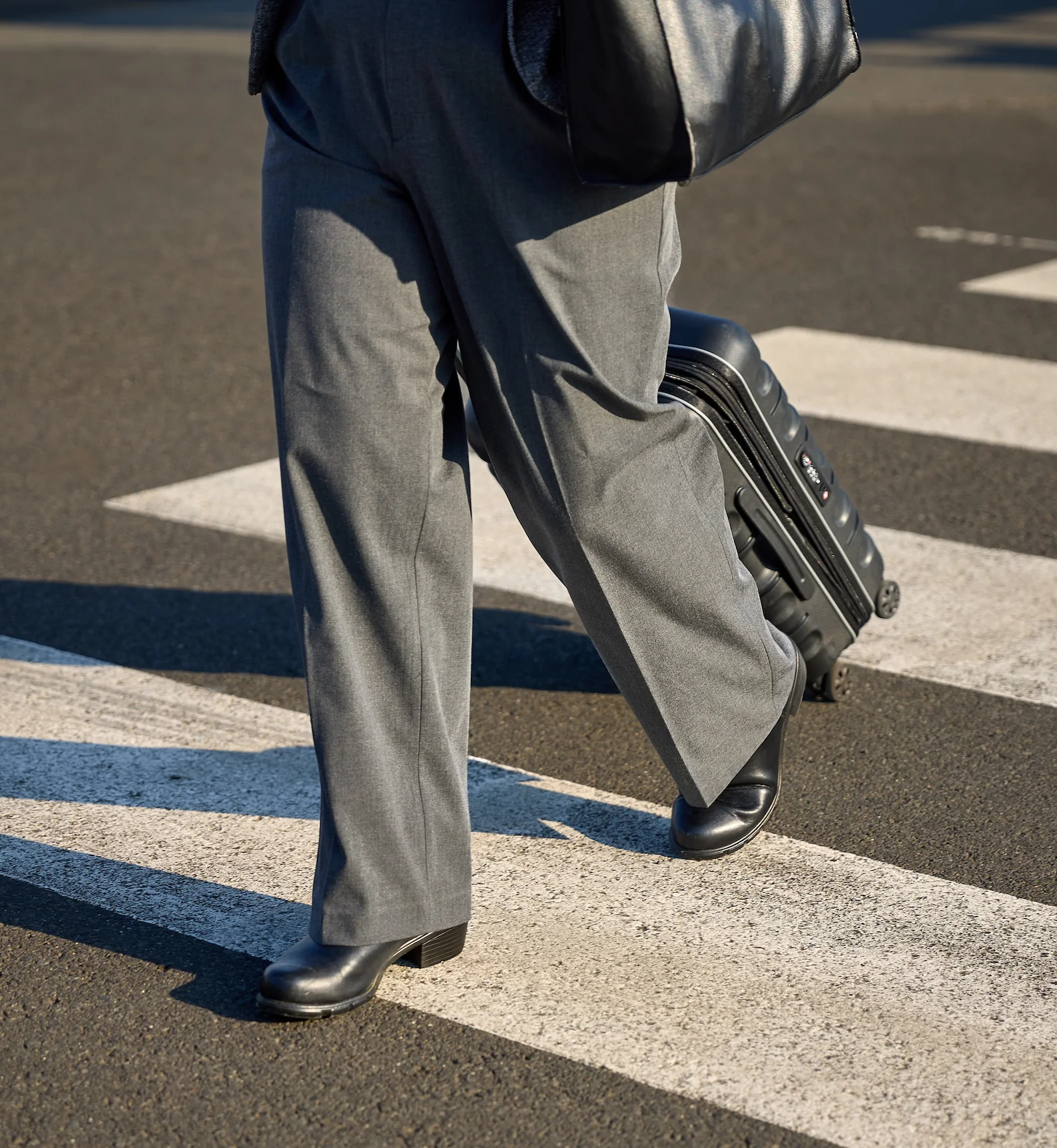 A business person walks across a zebra crossing with a suitcase