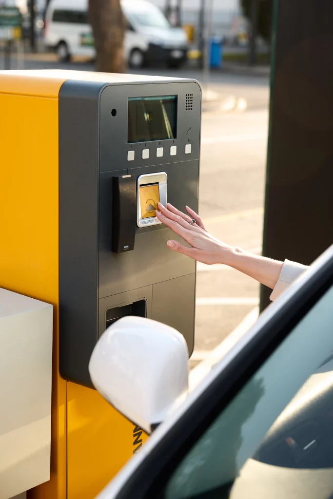 Someone reaching out of their car to interact with a ticketing machine