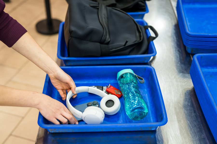 Blue security screening tray with travel items including headphones, drink bottle.